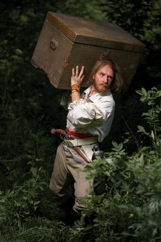 Sea robber ship captain armed pirate goes through jungle with chest of treasures. Concept historical halloween. Filibuster cosplay