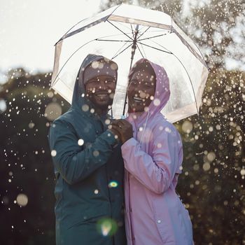 We love the rain. an affectionate couple standing under an umbrella while out in the rain.