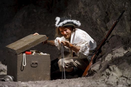 Sea robber captain of pirate ship armed with treasure chest in cave. Concept historical halloween. Filibuster cosplay