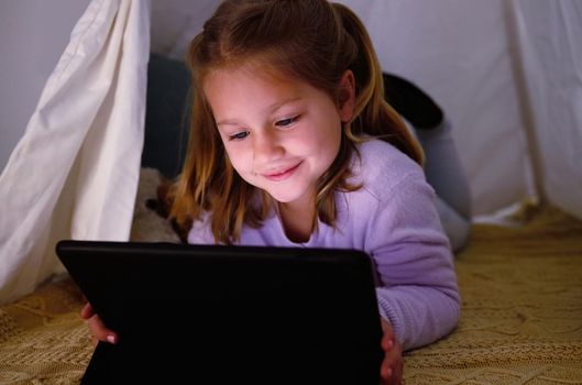 The characters in this story are so funny. an adorable little girl using a digital tablet at night.
