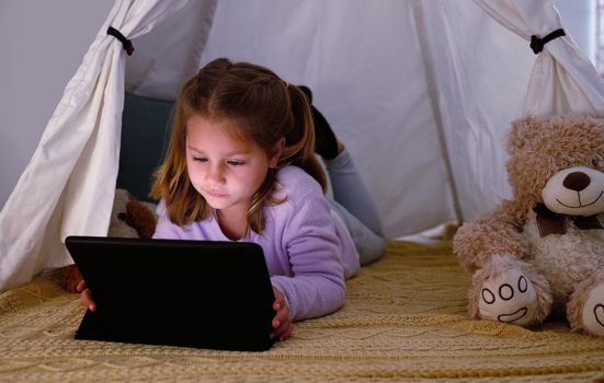 I have a few more minutes of screen time and cant decide what to watch. an adorable little girl using a digital tablet at night.
