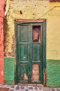 Old damaged wooden door of an abandoned weathered building. Vintage broken and aged green entrance to a house in a small village or town on a sunny day. Antique and rustic doorway of a vacant home