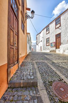 Scenic view of old historic houses, residential buildings, traditional infrastructure in cobblestone alleyway in a city street or road. Travel destination in Santa Cruz, La Palma, Spain