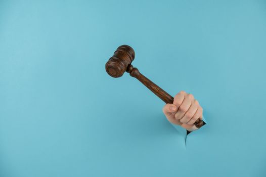 A woman's hand with a wooden judge's gavel sticks out of a hole in a blue background. Copy space.