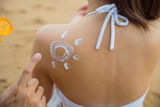 young man applying suntan lotion with sun shape on girlfriend back shoulder