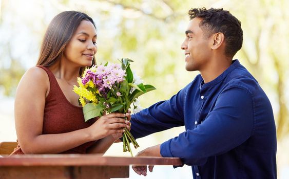 Making their date as romantic as possible. a handsome young man giving his girlfriend flowers during their date on a wine farm.