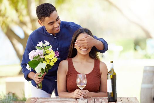 Guess who. a handsome young man surprising his girlfriend with flowers on a wine farm.