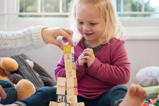 Lets add one more. a little girl stacking blocks with her mother at home.