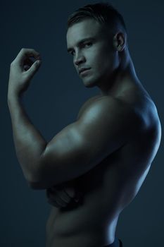 The picture of strength and masculinity. Studio portrait of a muscular young man posing shirtless against a dark background.