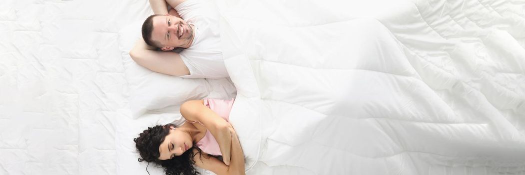 Wife and husband happily laying bed, white bedclothes