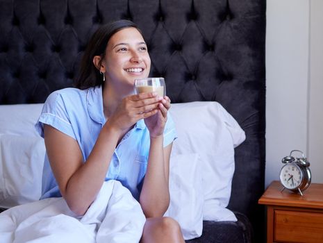 Starting the day off with a refreshing glass of water. a young woman drinking a glass of water in bed at home.