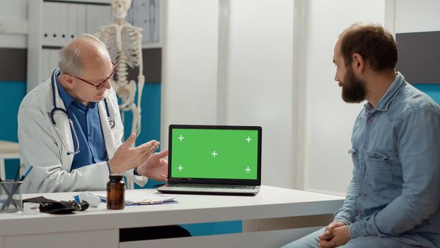 General practitioner pointing at laptop display with greenscreen