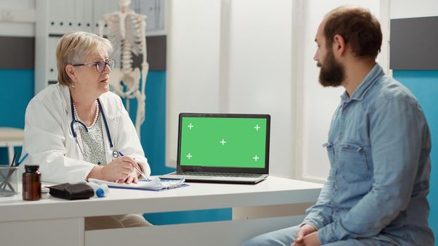 Senior doctor and patient looking at laptop with greenscreen