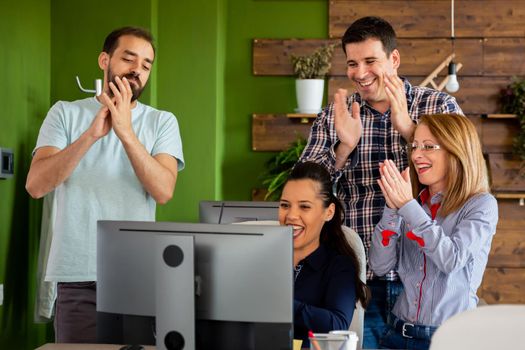 Young creative team in start-up company clapping in front of PC screen