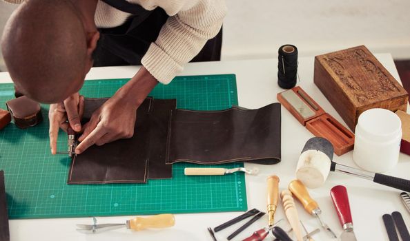 Skill and dedication. High angle shot of an unrecognizable male designer working with leather in his design studio.