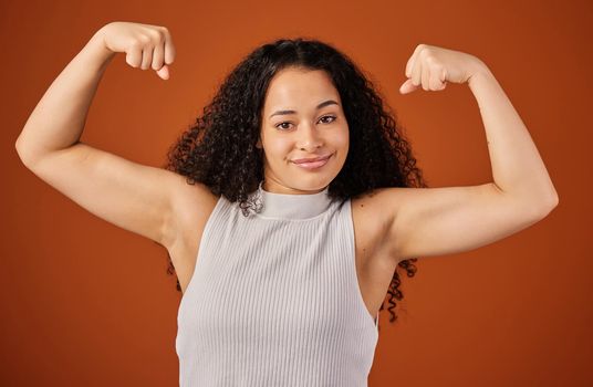 Individuality is power. Cropped portrait of an attractive young woman flexing her biceps in studio against a red background.