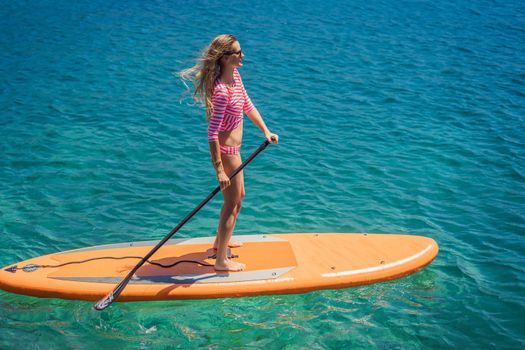 Young women Having Fun Stand Up Paddling in blue water sea in Montenegro. SUP. girl Training on Paddle Board near the rocks