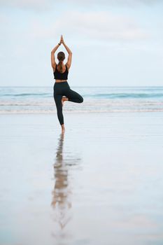 The steadiness in the tree pose helps you calm your mind. Rearview shot of a young woman doing a tree pose while practising yoga at the beach.