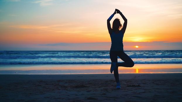 Silhouette Woman practice yoga tree pose to meditation with summer vacation beach happiness and relaxation. Calm female exercise with yoga meditate ocean beach with sunset golden time.