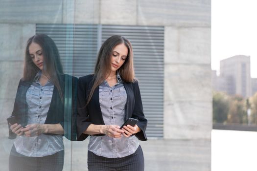 Business woman 35 years dressed stripe shirt and black jacket with long hair standing near office building outdoor use smartphone