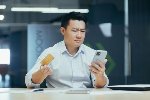 Frustrated Asian businessman with credit card and phone