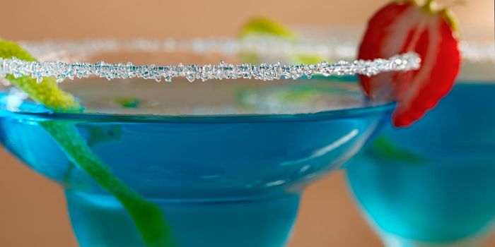 Two glasses with blue margarita cocktail garnished with lime zest and strawberries, selective focus