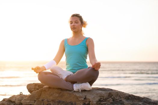 Woman practice yoga lotus pose to meditation with summer vacation rocky beach happiness and relaxation. Calm female exercise with yoga meditate ocean beach with sunset golden time.