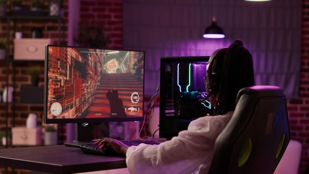 Over shoulder view of african american gamer girl playing online games using gaming pc setup