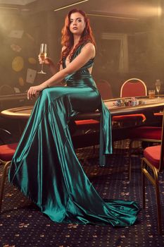 Young beautiful woman is posing against a poker table in luxury casino.