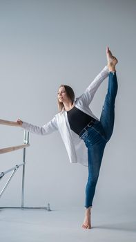 Caucasian woman in casual clothes pulls the longitudinal split at the ballet barre.