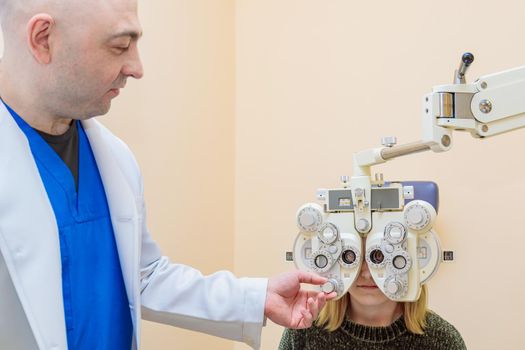 A male ophthalmologist checks a girl's eyesight using a phoropter. Vision treatment