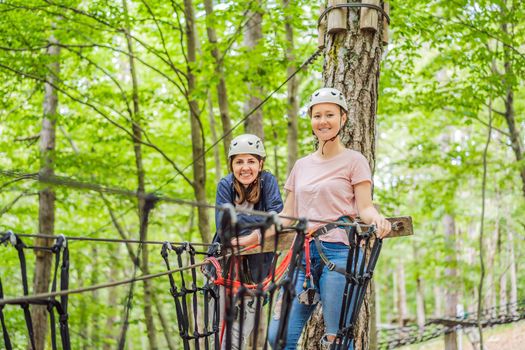 Two women girls female gliding climbing in extreme road trolley zipline in forest on carabiner safety link on tree to tree top rope adventure park. Family weekend children kids activities concept