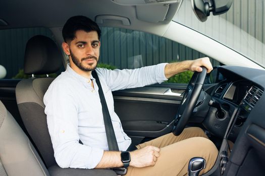 Portrait of handsome young businessman smiling while driving a new car. Young handsome man is sitting in luxury car. Bearded man is driving.