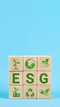ESG Words on a wood cubes. ESG concept of environmental, social and governance. Wooden cube with abbreviation ESG standing with other icons on blue background
