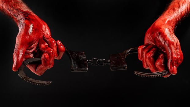 A man with bloody hands holds iron handcuffs.