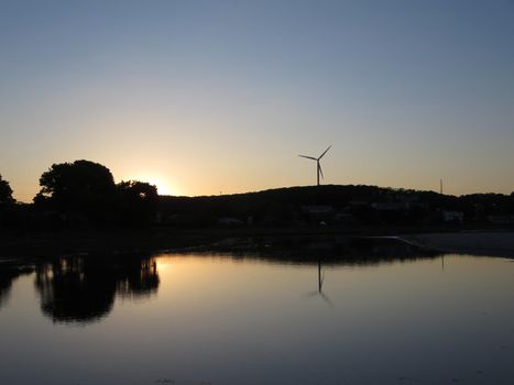 Sunsets over Stream leading to beach with windmill visible 