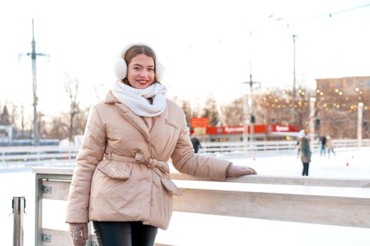 Beautiful lovely young adult woman brunet hair warm winter jackets stands near ice skate rink background Town Square. Christmas mood lifestyle
