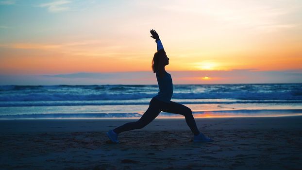 Silhouette Woman practice yoga warrior pose to meditation with summer vacation beach happiness and relaxation. Calm female exercise with yoga meditate ocean beach with sunset golden time.