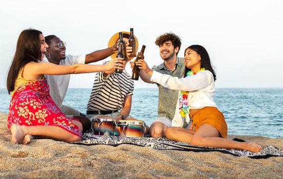 Happy, diverse group of friends toasting with beer together at the beach. Multiracial young people having fun outdoor.