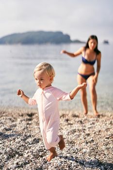 Little girl walks barefoot on a pebble beach