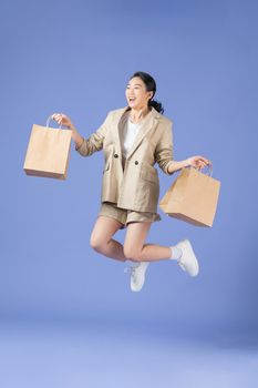 attractive happy girl jumping with shopping bags, isolated on purple