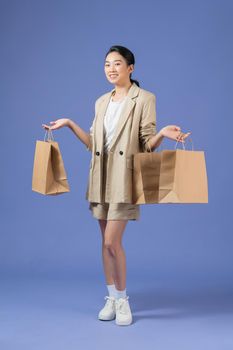 Happy young woman with shopping bags on purple background