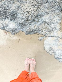 footed woman's legs standing on yellow sand on the beach with the big stone