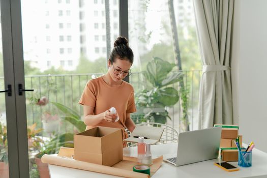 Woman packing cosmetic products in box for courier or poster shipment.