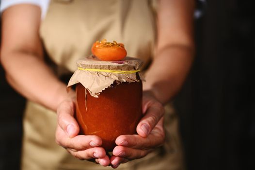 Details: A housewife holding a jar of homemade apricot jam. A juicy ripe apricot fruit on the lid
