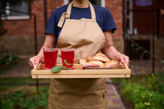 Housewife holds a serving tray with homemade cherry pies and drinking glasses with refreshing compote from cherries