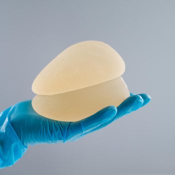 Doctor in a rubber glove holding a pile of breast implants.