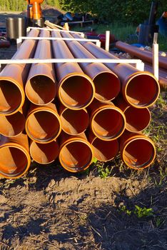 sewer orange pvc pipes stacked on construction site.
