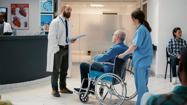 Male doctor meeting with old patient in wheelchair at reception lobby