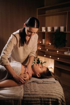 A masseuse gives a body massage to a woman in a spa center. A professional masseur massages the shoulder of a girl lying in a spa center.